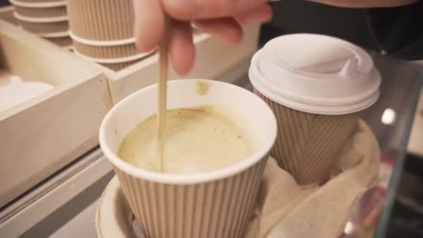 Mano revuelve azúcar con cuchara en taza desechable de café con leche de soja y cubrirlo con tapa de plástico . — Vídeos de Stock