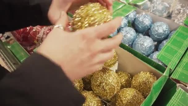 Bola dorada y brillante para el árbol de Navidad en manos femeninas. Chica elige nuevos juguetes de año . — Vídeos de Stock