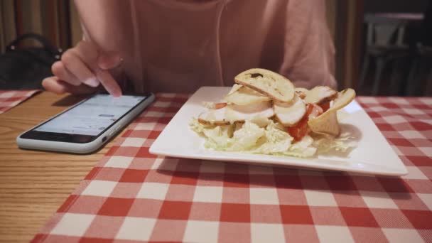 Hipster chica comiendo ensalada en el restaurante y mensajes de texto en el teléfono inteligente . — Vídeos de Stock