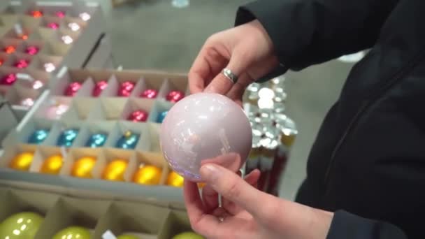 Женщина выбирает рождественские игрушки, держит в руках розовый шар . — стоковое видео