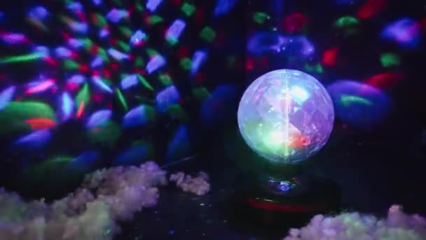 Uma pequena grinalda de bola de discoteca festiva gira em uma sala escura e projeta imagens abstratas na parede . — Vídeo de Stock