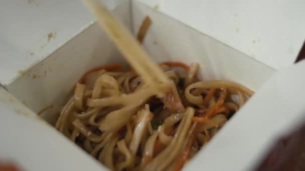Το κορίτσι αναμιγνύει udon με κοτόπουλο με ξύλινων chopsticks σε takeaway κουτί. — Αρχείο Βίντεο