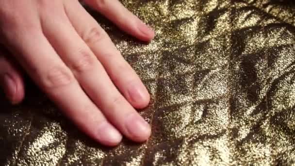 Vrouw aanraken van een gladde, gouden nylon polyester weefsel in een textiel-winkel. — Stockvideo