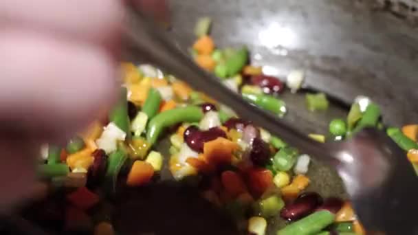 En person blandar vegetabilisk blandningen i en kokande olja i en Traktörpanna med en sked. — Stockvideo