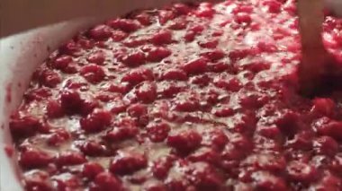 Kadın ahşap bir spatula ile emaye bir kase taze ahududu reçeli karıştırma.