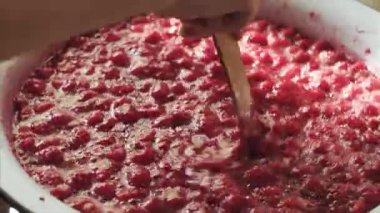 Ahşap bir spatula ile emaye bir kase içinde ahududu reçeli karıştırarak Kadın el.