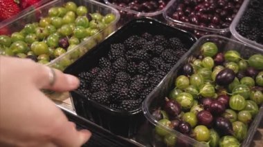 Vejetaryen kız süpermarkette mağaza tezgahında böğürtlen seçer. 