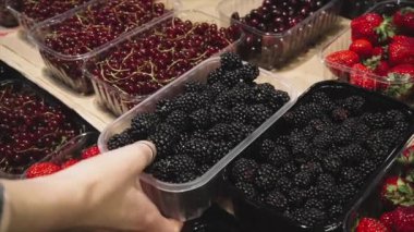 Vegan kız süpermarkette mağaza tezgahında taze organik böğürtlen seçer. 