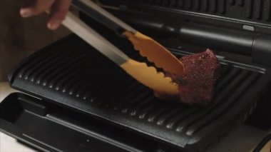 Adam elektronik ızgara biftek için taze baharatlı sığır eti bırakır.