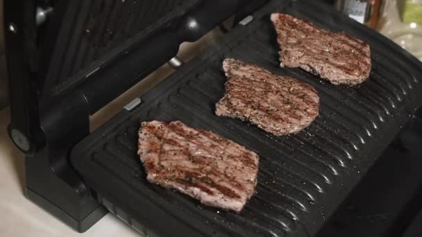 Bifes de carne suculentos médio raro em uma grade elétrica em casa . — Vídeo de Stock