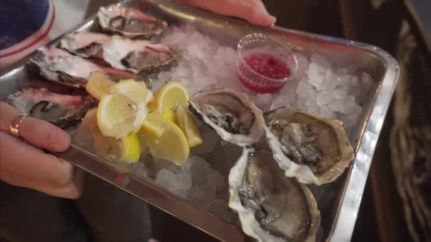 Huîtres fraîches de haute qualité sur un plateau avec glace, citron et sauce dans les mains d'une jeune fille . — Video