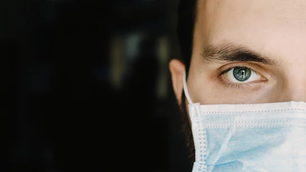 Portrait d'un jeune homme dans un masque médical regarde la caméra, pendant la pandémie de coronavirus. — Photo