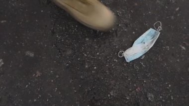 Kadın kaldırımda duran kullanılmış bir koruyucu maskeye basıyor..