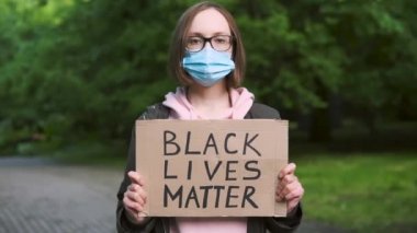 Koruyucu tıbbi maskeli bir kız, insan haklarını desteklemek için elinde bir karton tutuyor. Siyahların Yaşamı Önemlidir.