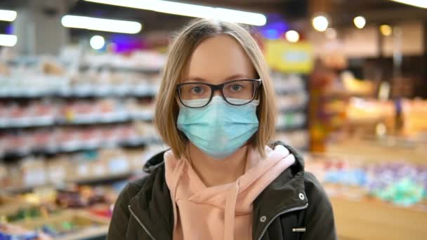 Retrato de una mujer con máscara de protección médica y gafas mira a la cámara . — Vídeos de Stock