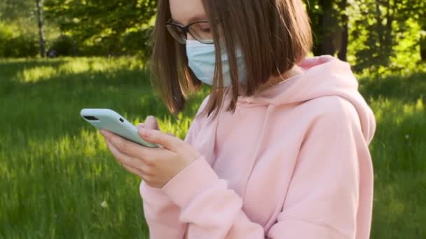 眼鏡や医療用マスクの女性は、スマートフォンのテキストメッセージを使用して、パンデミックニュースを検索. — ストック動画