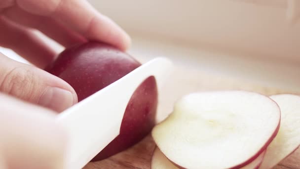 Um blogueiro corta uma maçã vermelha madura com uma faca de cerâmica em uma placa de corte para seu vídeo asmr enquanto em quarentena . — Vídeo de Stock