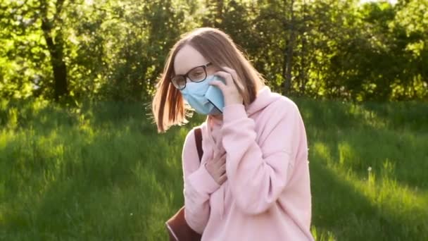 A girl in a protective mask talking on the phone in the street, in the park, in nature. — Stock Video