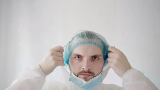 Ένας νεαρός καυκάσιος ιατρός επιδημιολόγος βάζει μια προστατευτική μάσκα στο πρόσωπό του. — Αρχείο Βίντεο