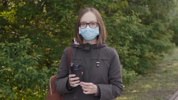 Mujer con una máscara médica con una taza de café en las manos. Imágenes de 4k . — Vídeo de stock