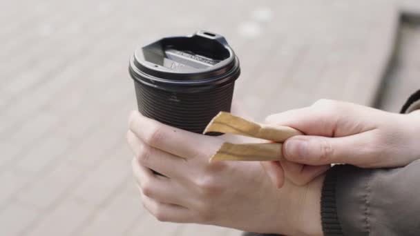 Una taza de café para llevar, edulcorante stevia se pega en las manos de una chica joven de cerca . — Vídeo de stock