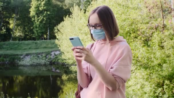 保護マスクの女性は、彼女のスマートフォンのテキストメッセージを使用して、ウェブサーフィン. — ストック動画
