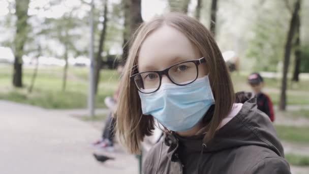 Ett porträtt av en ung trött flicka i en skyddande medicinsk mask på gatan närbild, slow motion. — Stockvideo