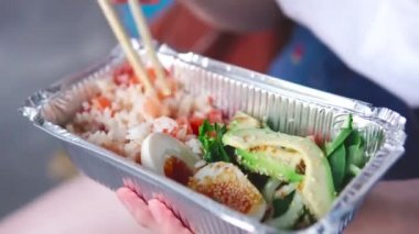 Kız yemek çubuklarıyla paket yemek yiyor: pirinç ve sebzeli somon kabı..