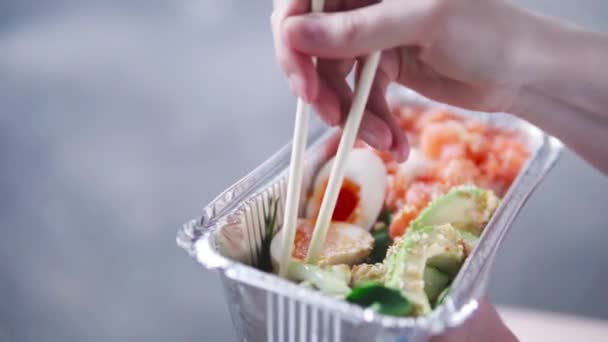 La chica mezcla arroz, pescado, huevos y verduras con palos, se come el golpe . — Vídeo de stock