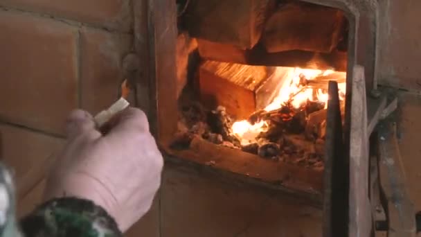 De gamla kvinnans händer lägger en logg i den brinnande spisen. — Stockvideo