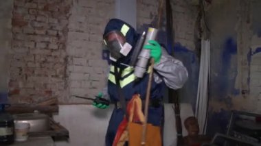 Tehlikeli madde ekipmanlı bir adam terk edilmiş fabrikada laboratuvar malzemelerini alıyor. Kapalı.