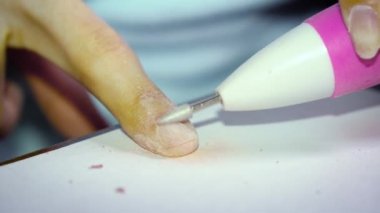 Çirkin tırnakları olan bir kız maniküre hazırlanmak için tırnak cilasını özel bir makineyle söker. Yakın çekim.