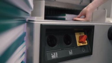 Matbaa işçisi kesme makinesi kullanıyor. İşçi tipografide bir yığın kağıt kesiyor.