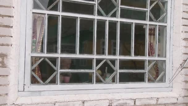 Опса, Беларусь, февраль 2019 года. Пожилой человек сидит за старым столом, пьет горячий напиток и смотрит в окно. — стоковое видео