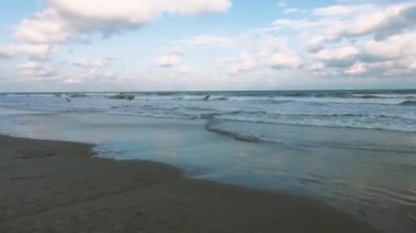 Güneş ufukta batarken dalgalar yavaşça kumlu bir sahile çarpıyor.