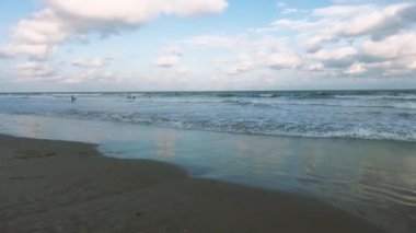 Güneş ufukta batarken dalgalar yavaşça kumlu bir sahile çarpıyor.