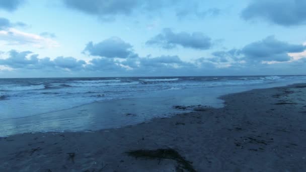 Κύματα πέφτουν απαλά σε μια αμμώδη παραλία καθώς ο ήλιος δύει στον ορίζοντα — Αρχείο Βίντεο