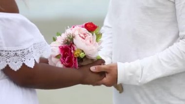 Yeni evli çift düğün gününde el ele tutuşuyorlar. Sahilde uluslararası çift.