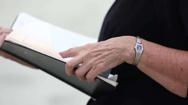 Close up view of two white female hands holding thick black book. Wedding organizer reading a book at a wedding in front of the newlyweds on the beach — Stock Video