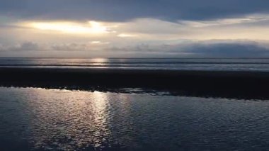 Güneş ufukta batarken dalgalar yavaşça kumlu bir sahile çarpıyor.