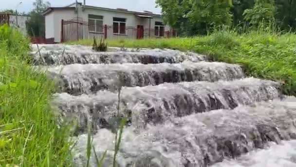 Vatten rinner nerför trappan mot byggnadens bakgrund. Regndroppar faller, översvämmar gatan. Vägöversvämningar under våta årstider. Översvämningar efter svåra åskväder och kraftigt regn 4k — Stockvideo