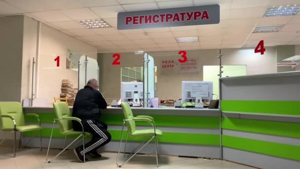 08.09.2020 Minsk, Bielorussia. In ospedale alla reception Infermiera in servizio parla con paziente e guida i suoi dati nel computer. Un medico in maschera e guanti protettivi passa davanti ai pazienti 4k — Video Stock