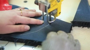 Dikiş imalatında çalışan kadın işçi elektrikli kumaş makinesi kullanıyor. Üretim hattı dikiyorum. Kıyafet tasarımcısı. Kadın elleri kumaş üzerinde çalışıyor. İşindeki terzi.