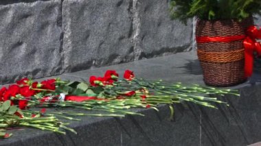 İnsanlar, şehit düşmüş Sovyet askerlerinin isimleriyle anıtın duvarına taze kırmızı çiçekler seriyorlar. Zafer Günü, anıların duvarına çiçek koyma geleneğidir. Karanfiller ve diğer çiçekler