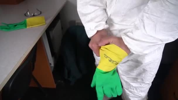 Ένας άντρας με λευκή στολή κατά της πανούκλας φοράει κίτρινα-πράσινα προστατευτικά γάντια στο εργαστήριο. Ακτινοβολία και μόλυνση. Πρόληψη της εξάπλωσης πανδημιών και ιών. Covid-19 — Αρχείο Βίντεο