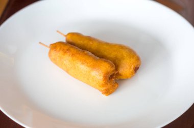 Beyaz tabakta Mısır. Sosis mısır unu hamur kalın bir tabaka kaplı bir sopa.