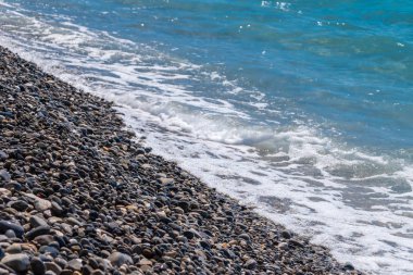 Deniz kıyısında küçük çakıl taşları üzerinde yumuşak dalgalar.