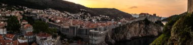 Sarı ve turuncu gökyüzü gündoğumu görünümü tarihi kent yüksek bir noktadan mesafe tepelerde taş duvarlarla çevrili Dubrovnik Hırvatistan üzerinden bakan muhteşem Panoraması.