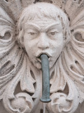 Closeup photograph of an old historic fountain caricature face of a child with floral decorative surrounding protruding from a white masonry stone wall in Dubrovnik Croatia. clipart