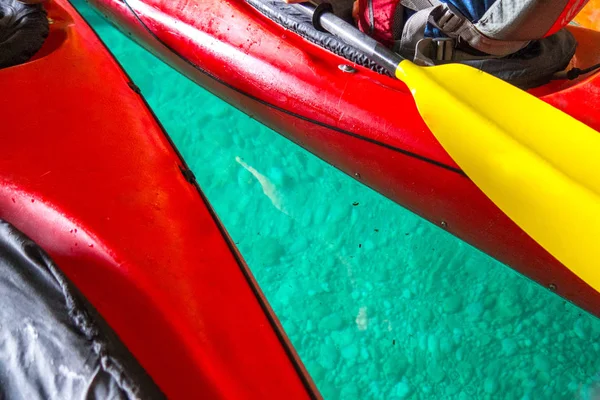 Close up colorful photograph of two red kayaks and yellow paddle on clear blue or green water with rocks on the bottom of the Adriatic Sea making a great sports or recreation background.